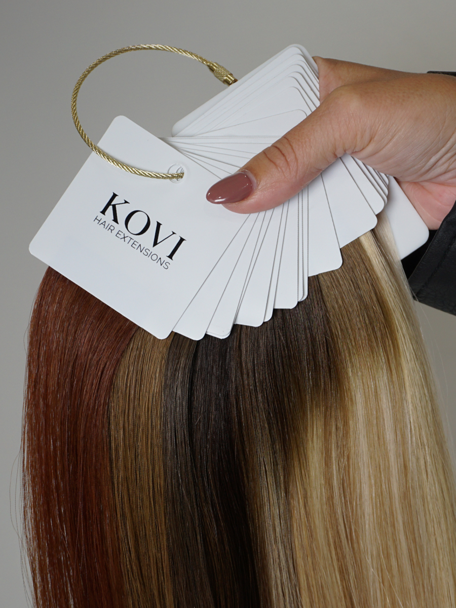  A set of new hair extension color swatches from the KOVI Hair color ring, showcasing a variety of rich, dimensional shades. Each swatch represents a unique hue, ranging from warm blondes to deep brunettes, ensuring a seamless match for every hair type. The high-quality human hair samples are neatly arranged on a ring for easy comparison and selection.